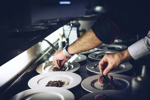 Hände beim Anrichten von Tellern an einer Restaurantküche
